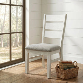 Homestead Dining Chair with a white-painted timber ladder-back frame and padded grey fabric seat, shown beside a window in a coastal-style room - The A2Z Furniture