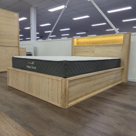 Canberra gas lift bed frame in pale oak, angled view on the showroom floor showing the fluted base panels and headboard - The A2Z Furniture showroom