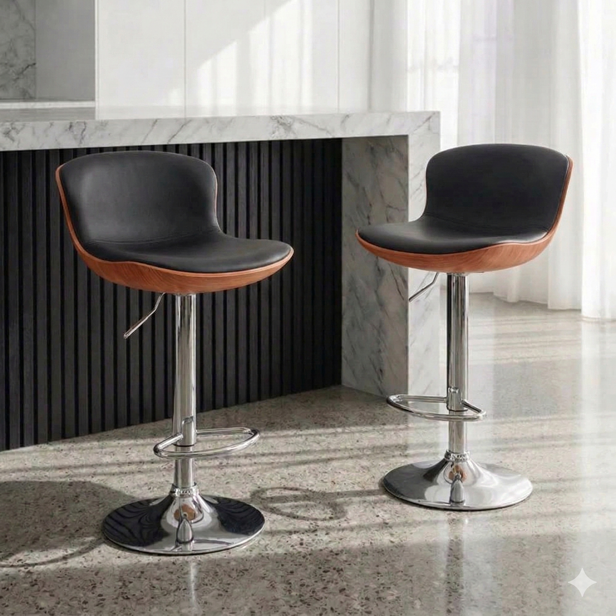 A pair of modern barstools with curved black fabric seats and walnut-finished wood bases are positioned in front of a contemporary kitchen island. The stools feature polished chrome pedestals with round bases and integrated footrests. The island showcases a white and grey marble countertop and waterfall side, accented with dark, fluted wooden panels beneath. 