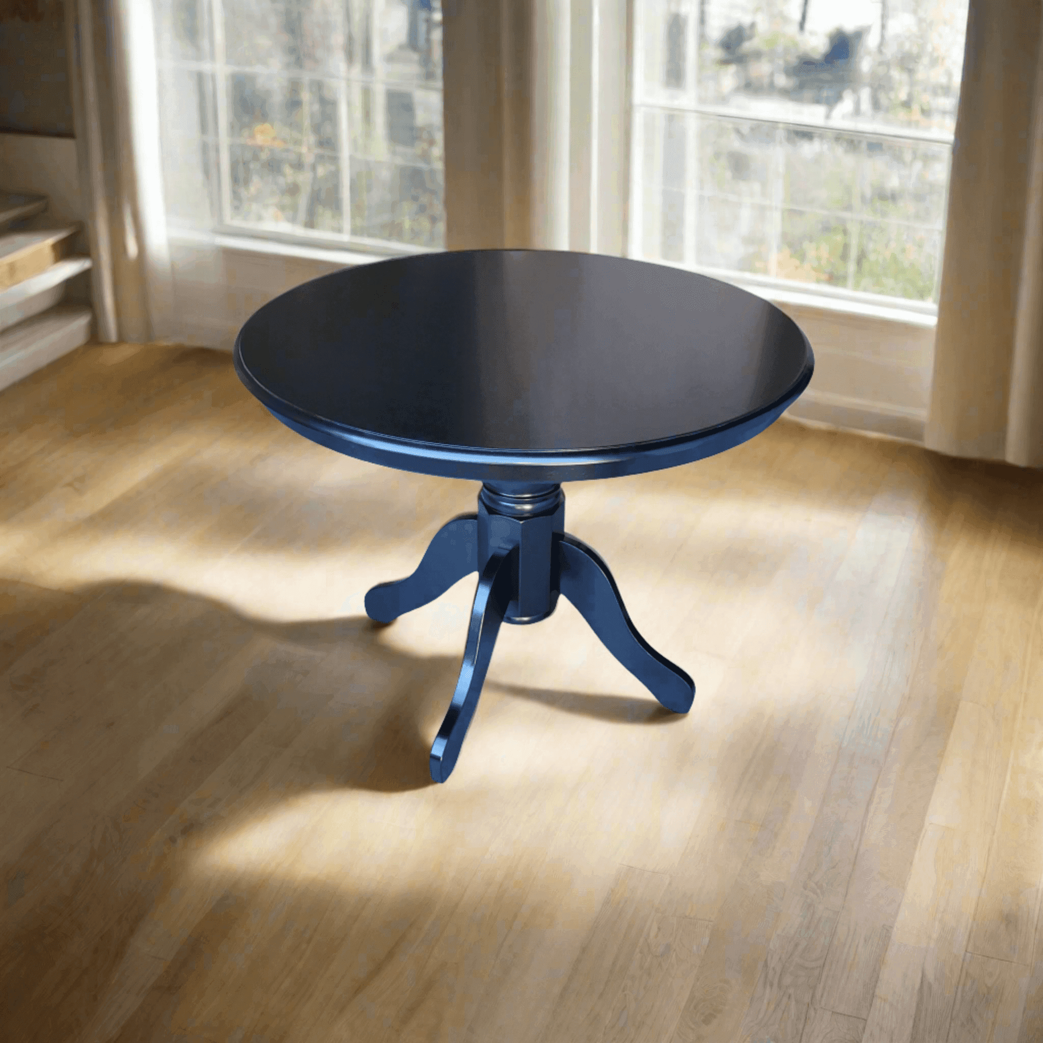 Round black wooden dining table with pedestal base on light wood floor in sunlit room