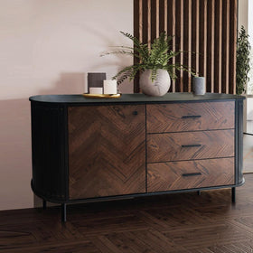 Modern wooden sideboard with black accents, herringbone doors, drawers, and decorative plants.
