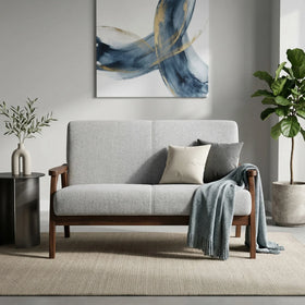 Donald 2 Seater Fabric Sofa in light grey with wooden frame, styled with cushions and throw in a modern living room setting featuring abstract wall art and indoor plants.