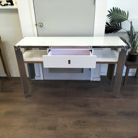 Modern console table with glass top, open drawer, and chrome legs, indoor setting