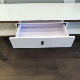 Modern white console table with glass top, open drawer, and chrome legs on wooden floor
