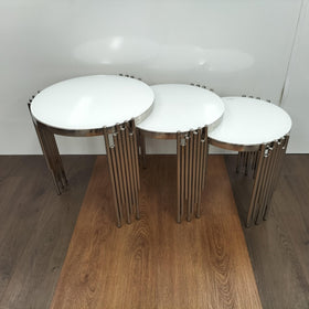 Set of three round white nest tables with chrome legs on wooden floor
