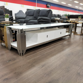 Modern white TV unit with glass top, metal accents, and storage drawers in a furniture showroom