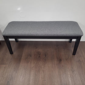 Modern grey upholstered dining bench with black wooden legs on wooden floor