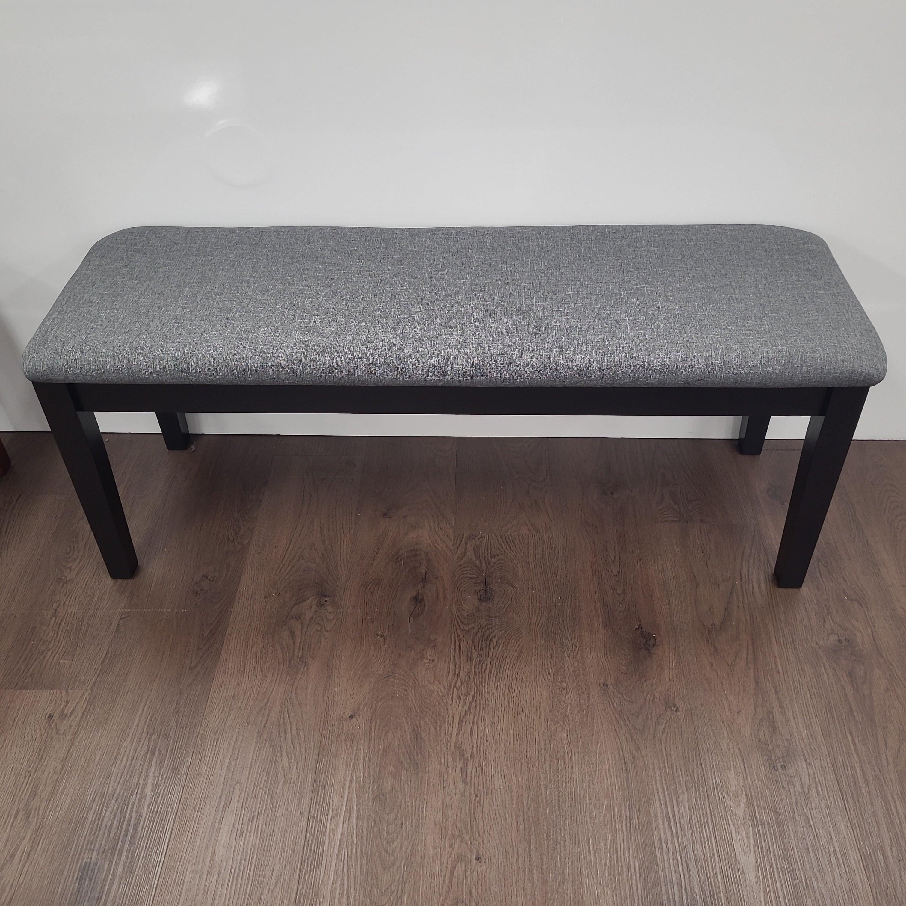 Modern grey upholstered dining bench with black wooden legs on wooden floor