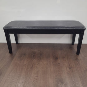 Modern black dining bench with padded seat on wooden floor against white wall