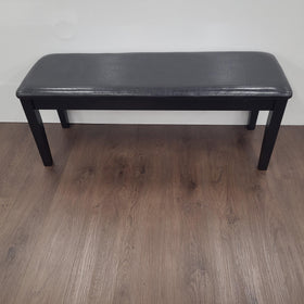 Modern black dining bench with cushioned seat on wood floor against white wall
