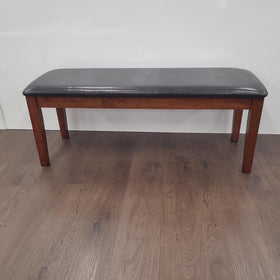 Rectangular dining bench with dark faux leather seat and wooden legs on timber flooring