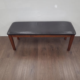 Modern dining bench with black upholstered seat and wooden legs on timber flooring