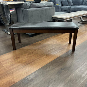Modern wooden dining bench with dark cushioned seat on wood flooring in a showroom