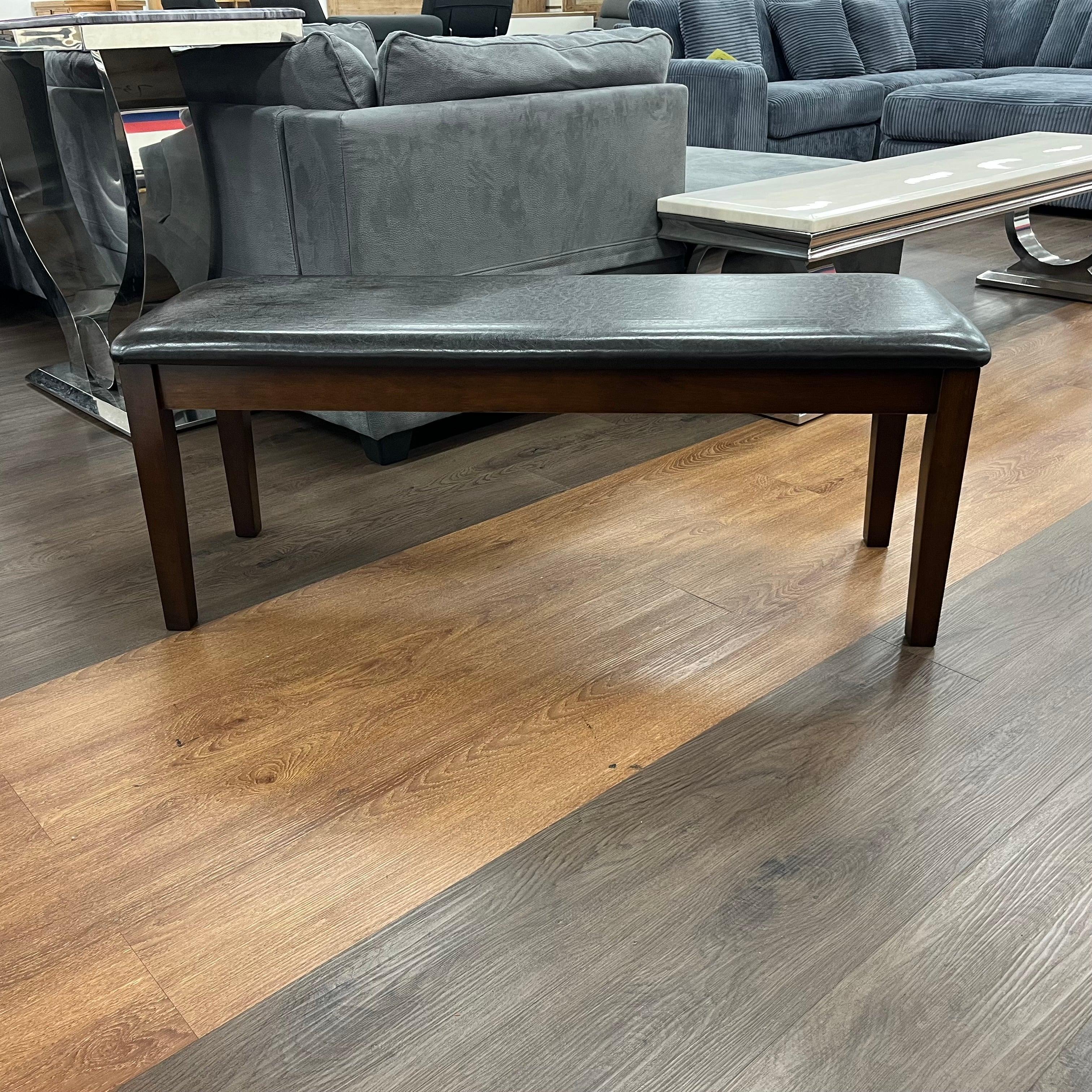 Modern wooden dining bench with dark cushioned seat on wood flooring in a showroom