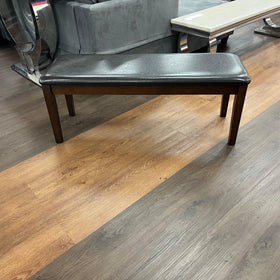 Dark brown wooden dining bench with padded seat on showroom floor