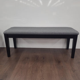 Modern dining bench with grey upholstered seat and black wooden legs on wood floor