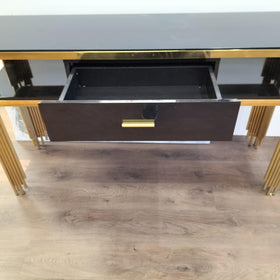Modern console table with black drawer, gold handles, and gold metal legs on wooden floor