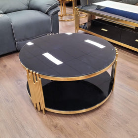 Round black glass coffee table with gold metal frame on wooden floor in modern living room