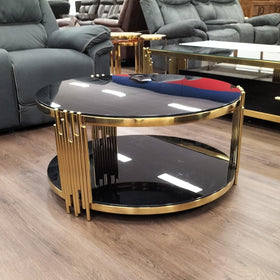 Round black glass coffee table with gold metal accents in a modern living room setting