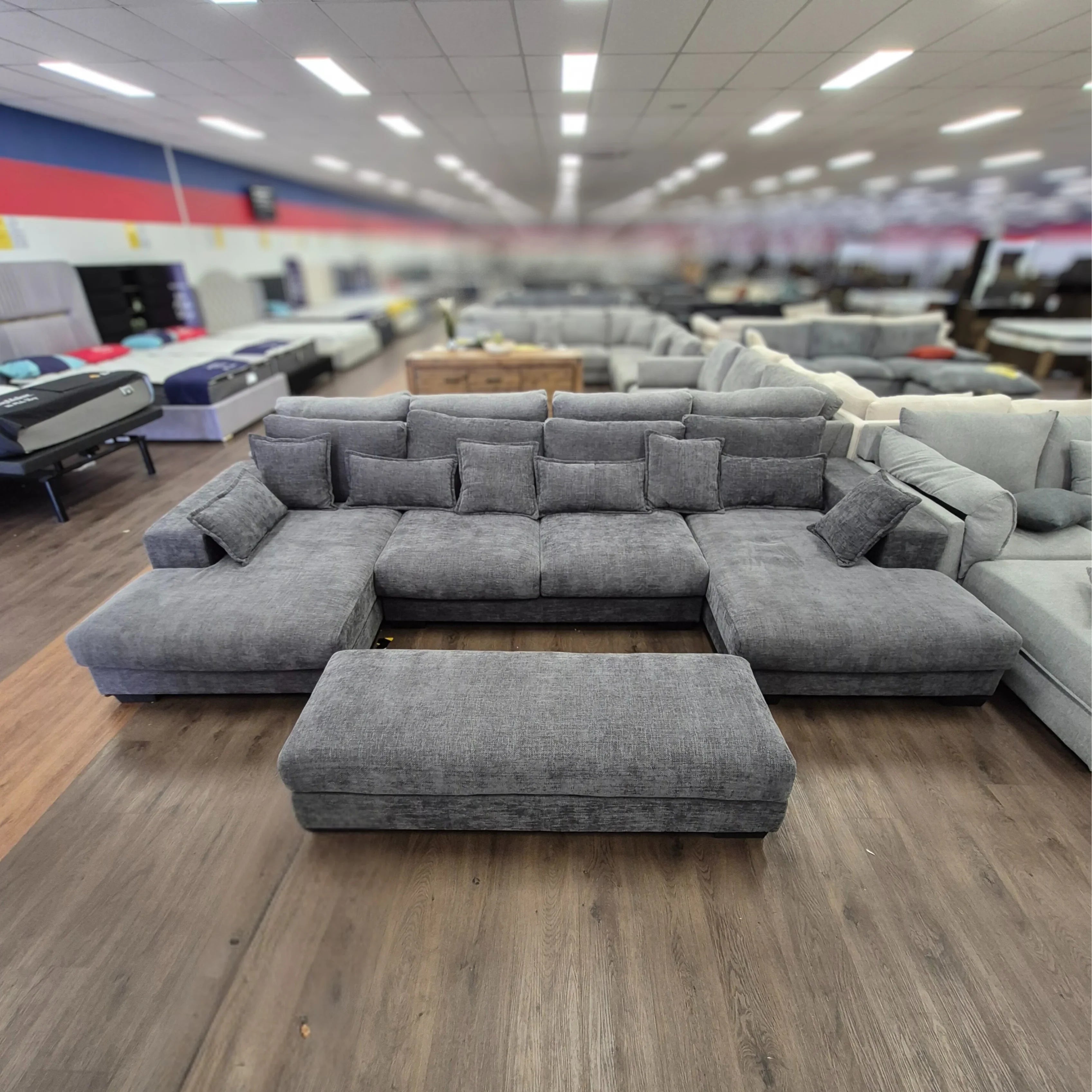 Large grey corner sofa with matching ottoman on wooden floor in showroom