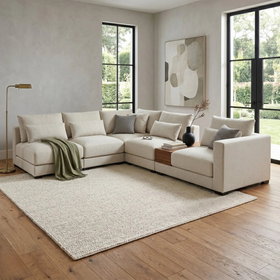 Beige sectional sofa in a modern living room with large windows and a rug.