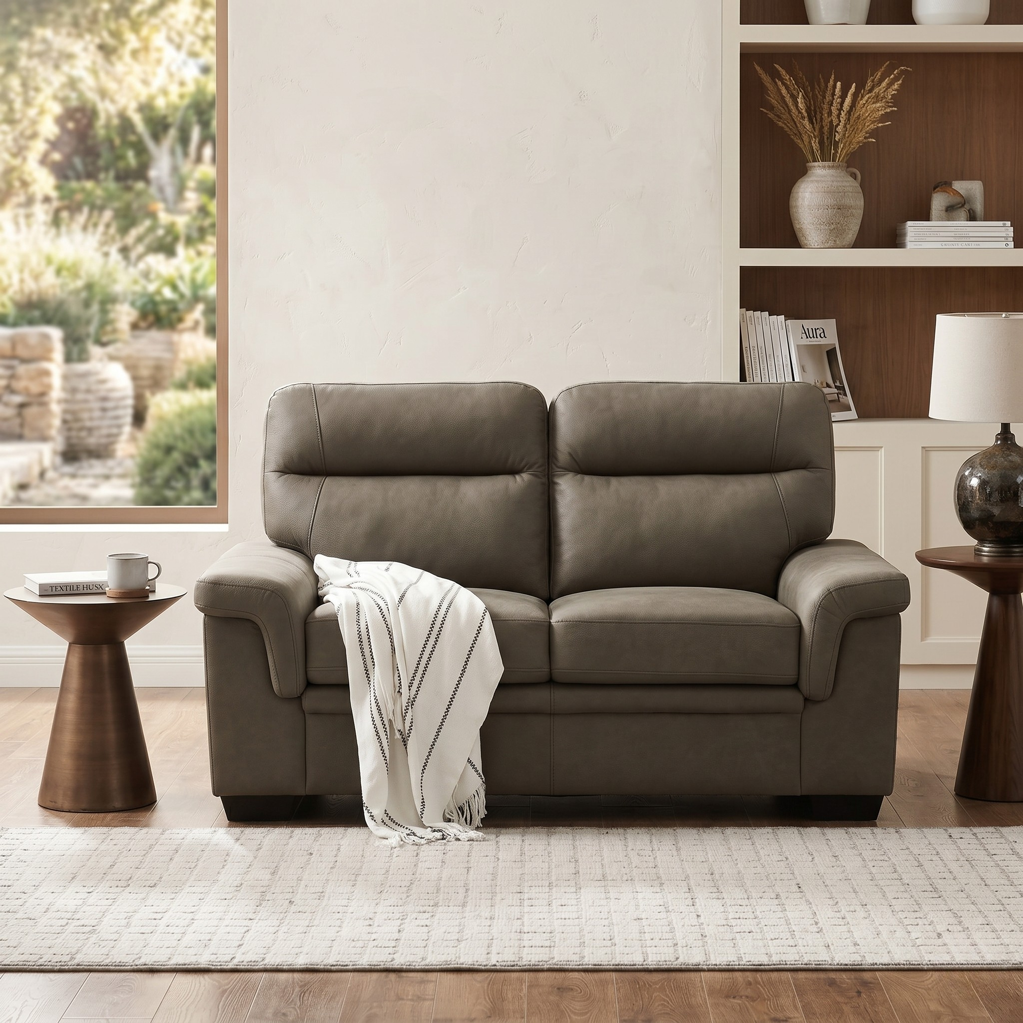Erika 2 Seater Fabric Sofa in gray with plush cushions and a cozy throw blanket, placed in a modern living room with natural light and wooden side tables.