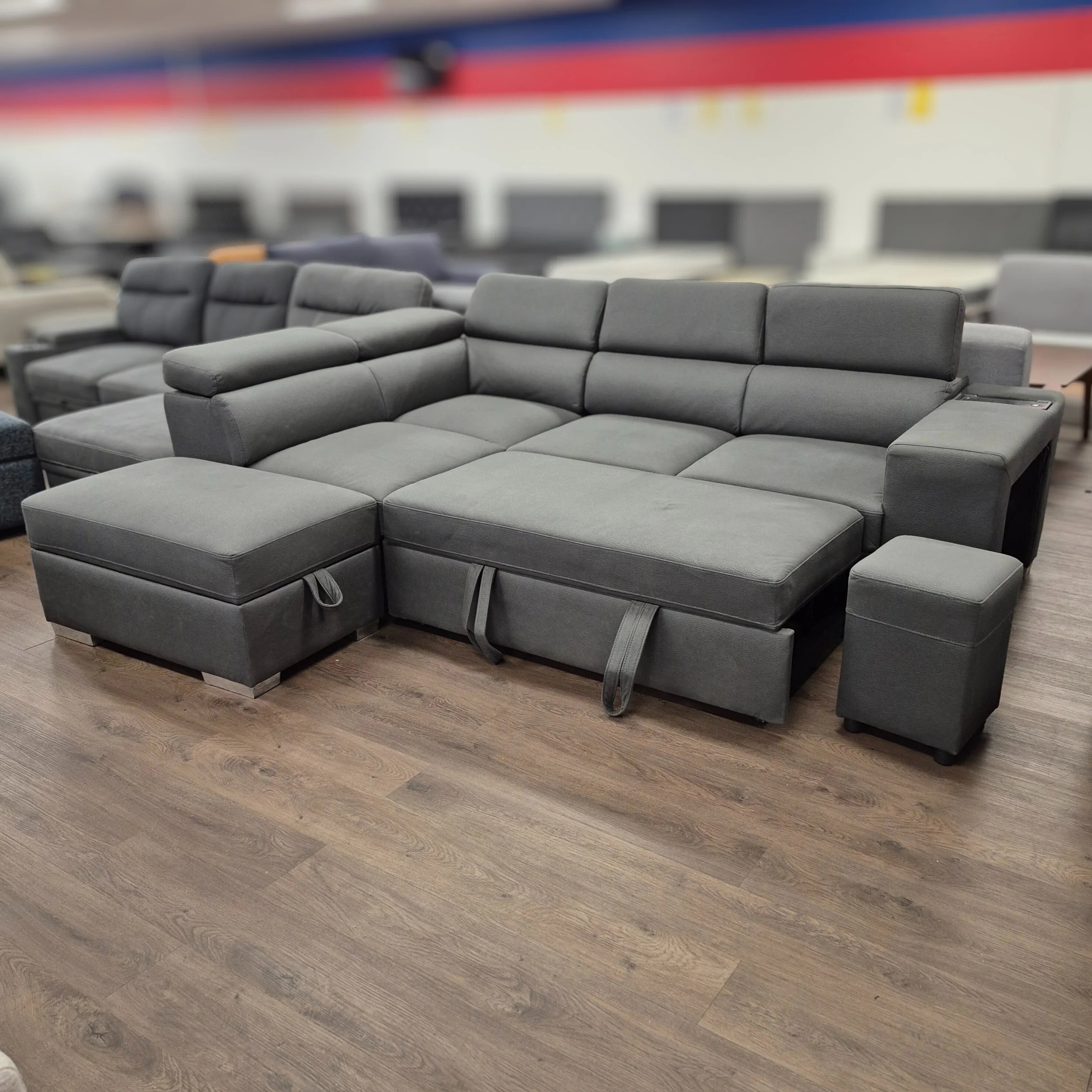 Gray pull-out sofa bed sectional with ottoman in a furniture showroom on wood flooring