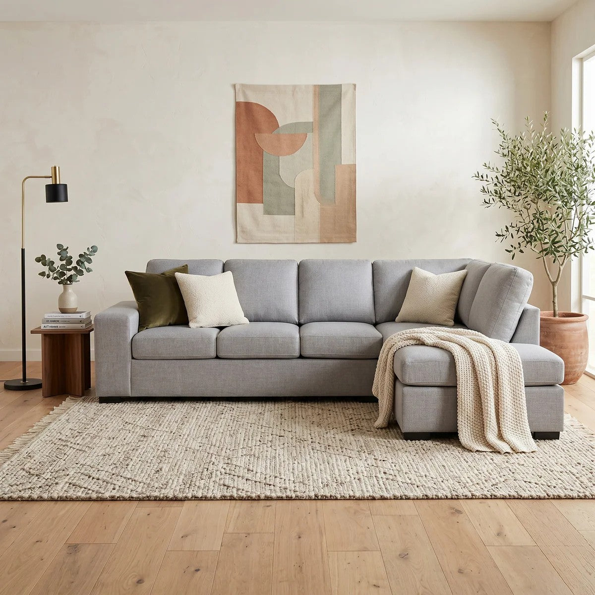 Fairfield Corner Sofa in light gray fabric with plush cushions, styled with neutral throw pillows and a cozy beige blanket in a minimalist living room setting.