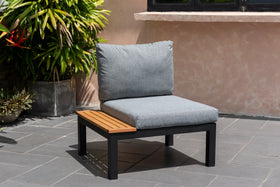 Modern outdoor lounge chair with grey cushions, black frame, and side teak table on patio