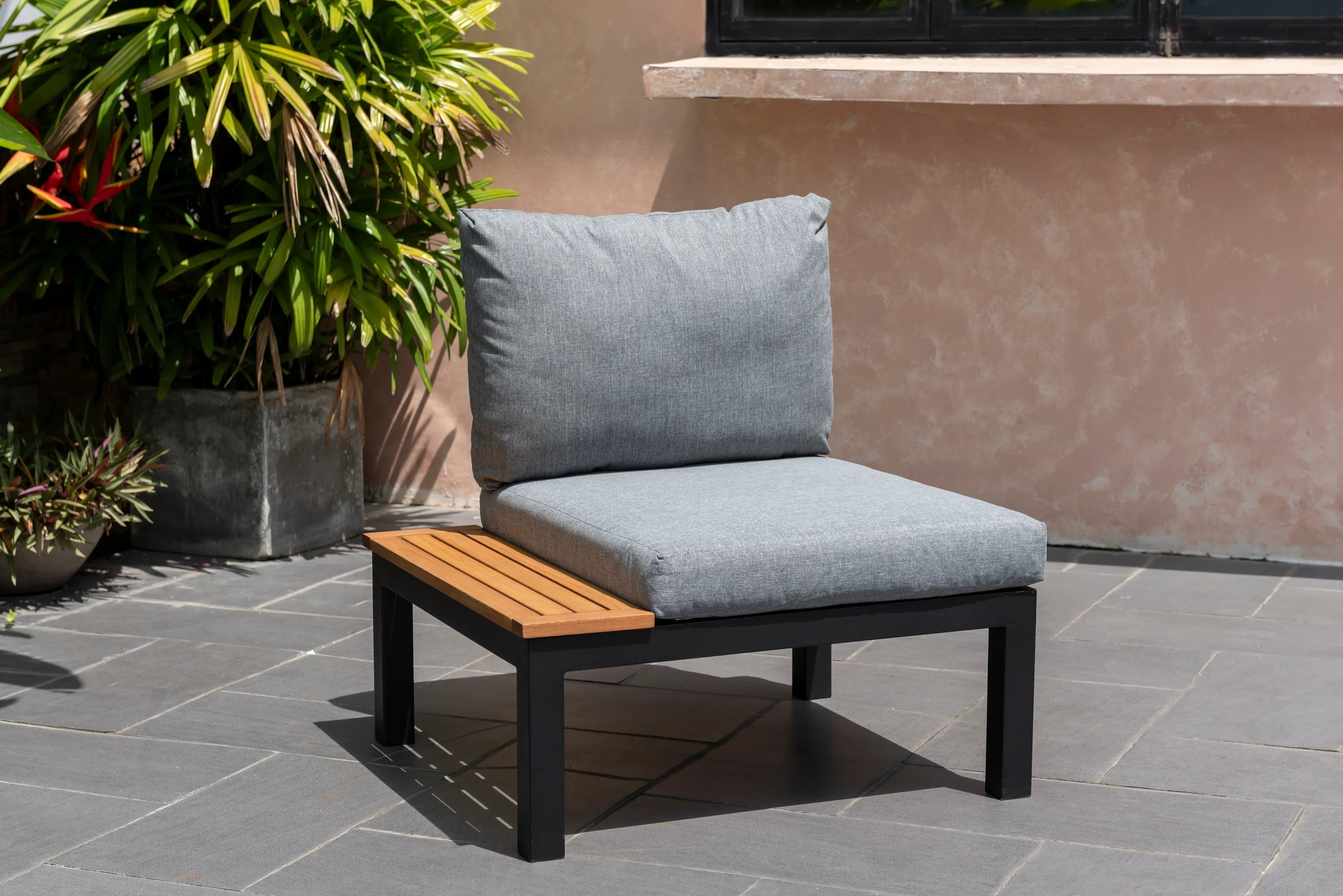 Modern outdoor lounge chair with grey cushions, black frame, and side teak table on patio