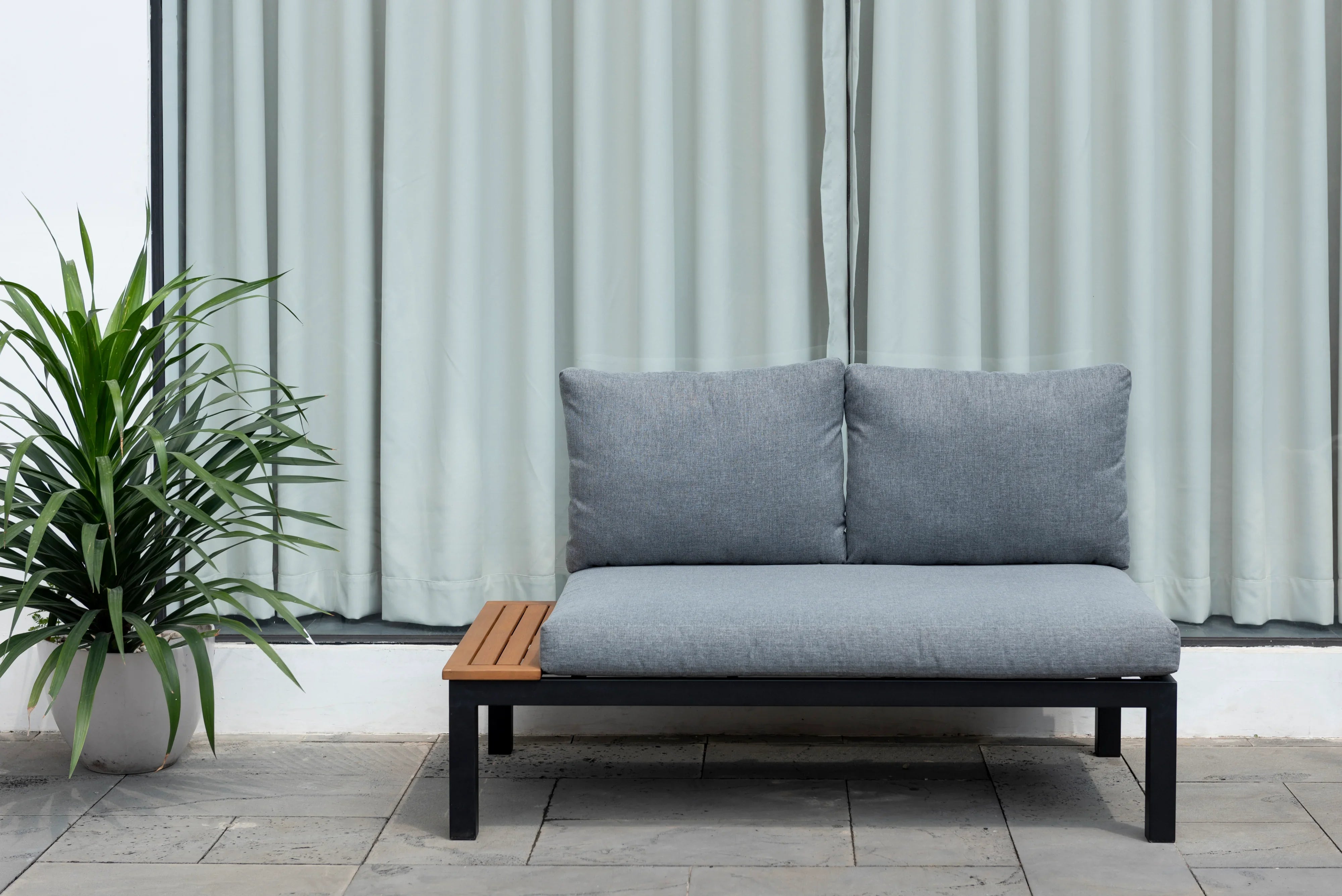 Modern grey outdoor 2-seater sofa with metal frame and wood detail, next to potted plant