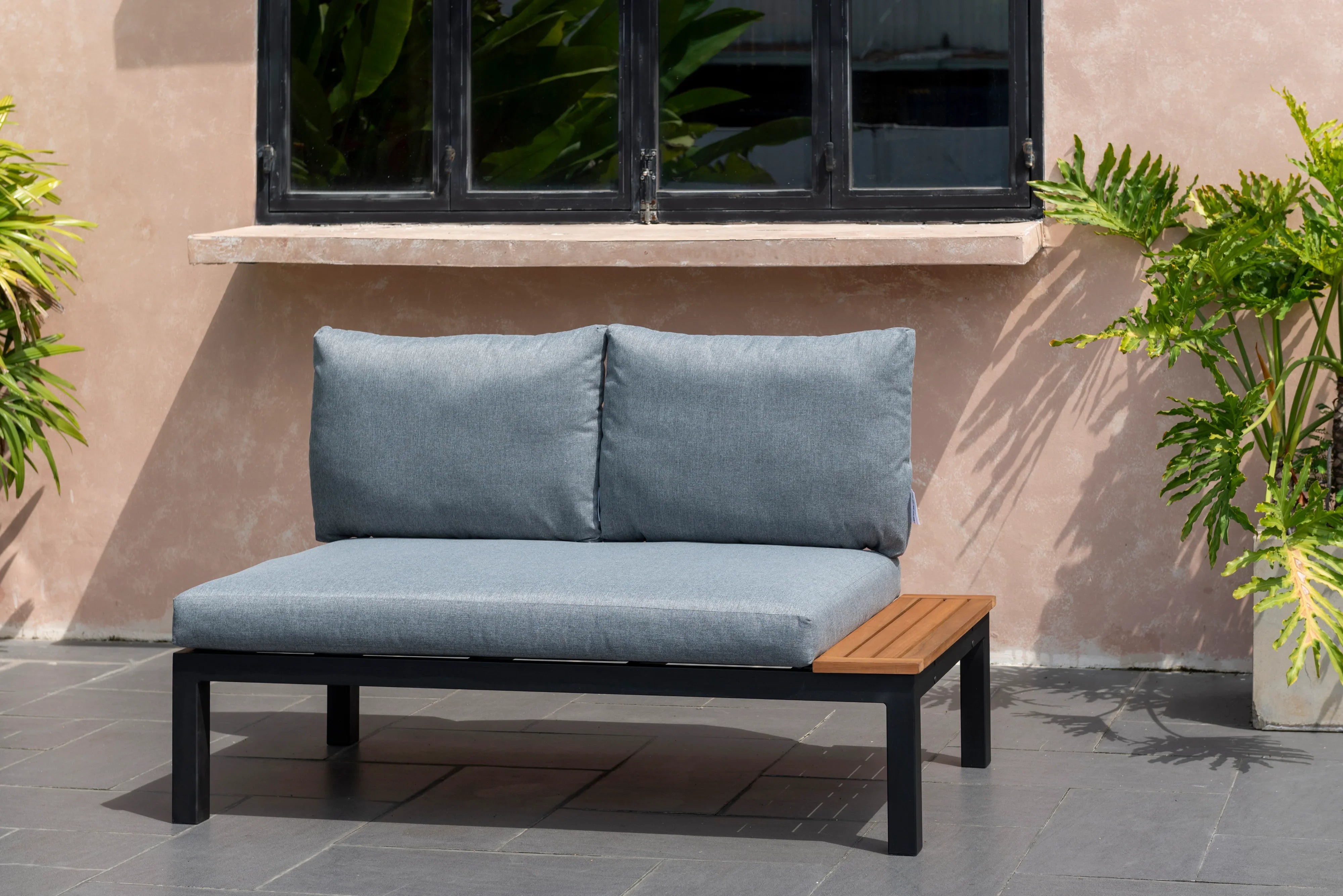 Modern outdoor two-seater grey sofa with wood side table on patio, plants beside