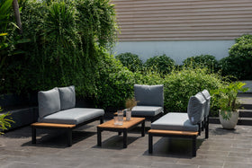 Modern outdoor lounge set with grey cushions and wooden table on a patio with lush greenery