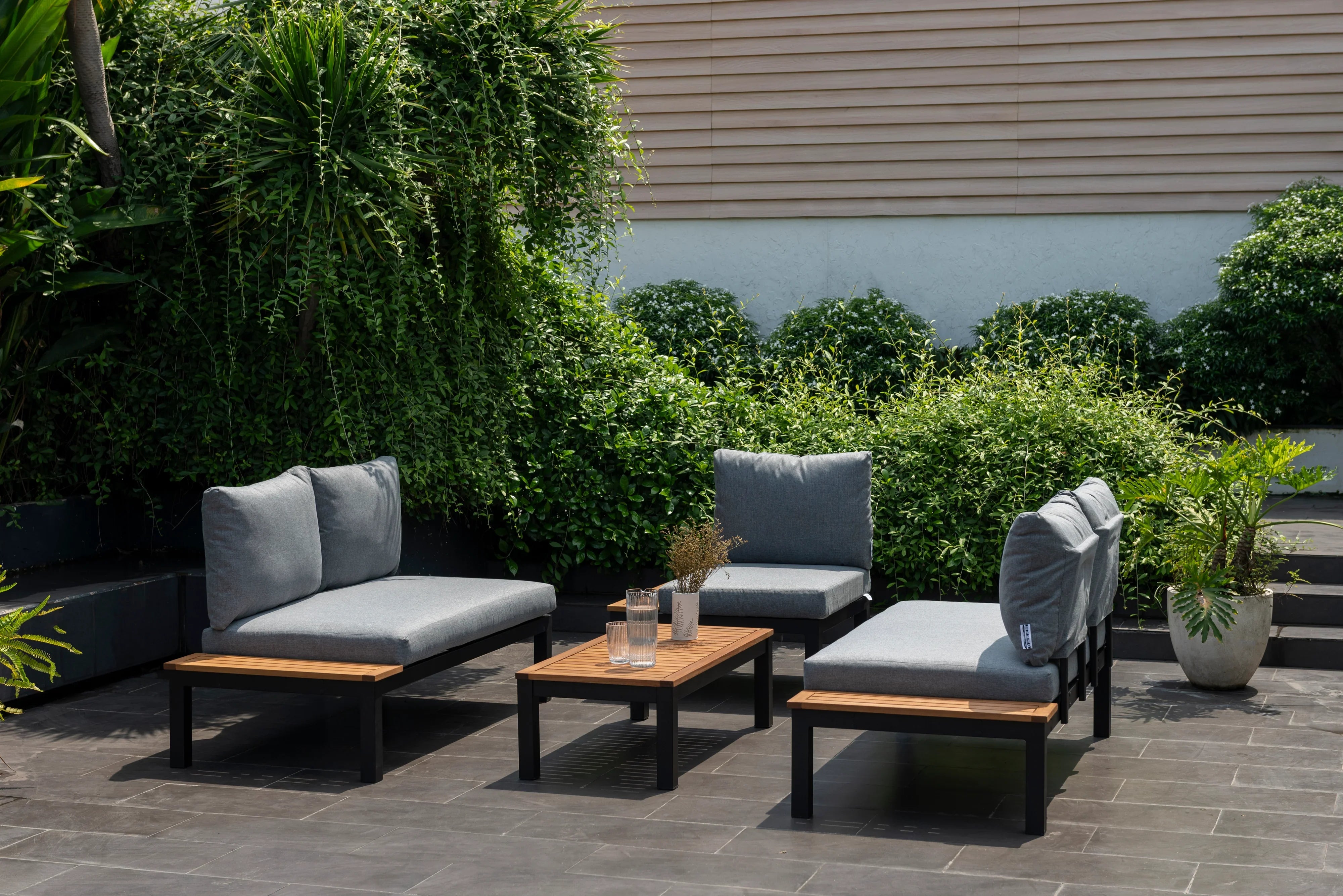 Modern outdoor lounge set with grey cushions and wooden table on a patio with lush greenery