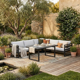 Outdoor patio with a sectional sofa, table, and decorative items in a garden setting.