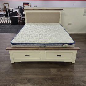 Jericho II Bed Frame with Storage, three-quarter angle view showing cream painted timber frame, walnut-toned wood top rails and oatmeal upholstered headboard panel, with a mattress on top, in The A2Z Furniture showroom