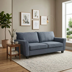 Modern living room setting featuring a blue Kensington 3 Seater Fabric Sofa next to a wooden side table with decor, plants, and framed minimalist art on the wall.