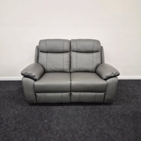 Dark grey leather two-seater recliner sofa with padded arms and backrest on carpeted floor