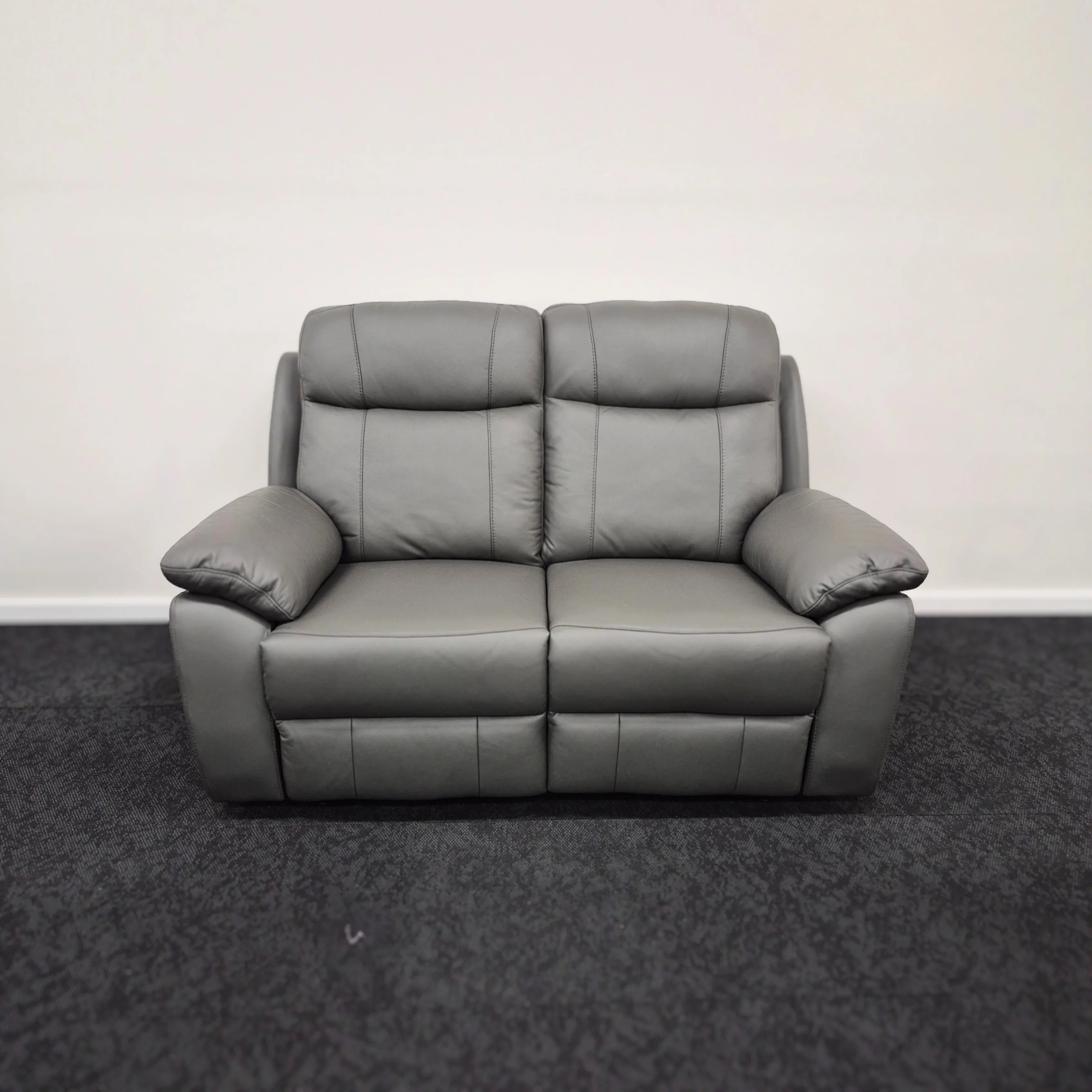 Dark grey leather two-seater recliner sofa with padded arms and backrest on carpeted floor