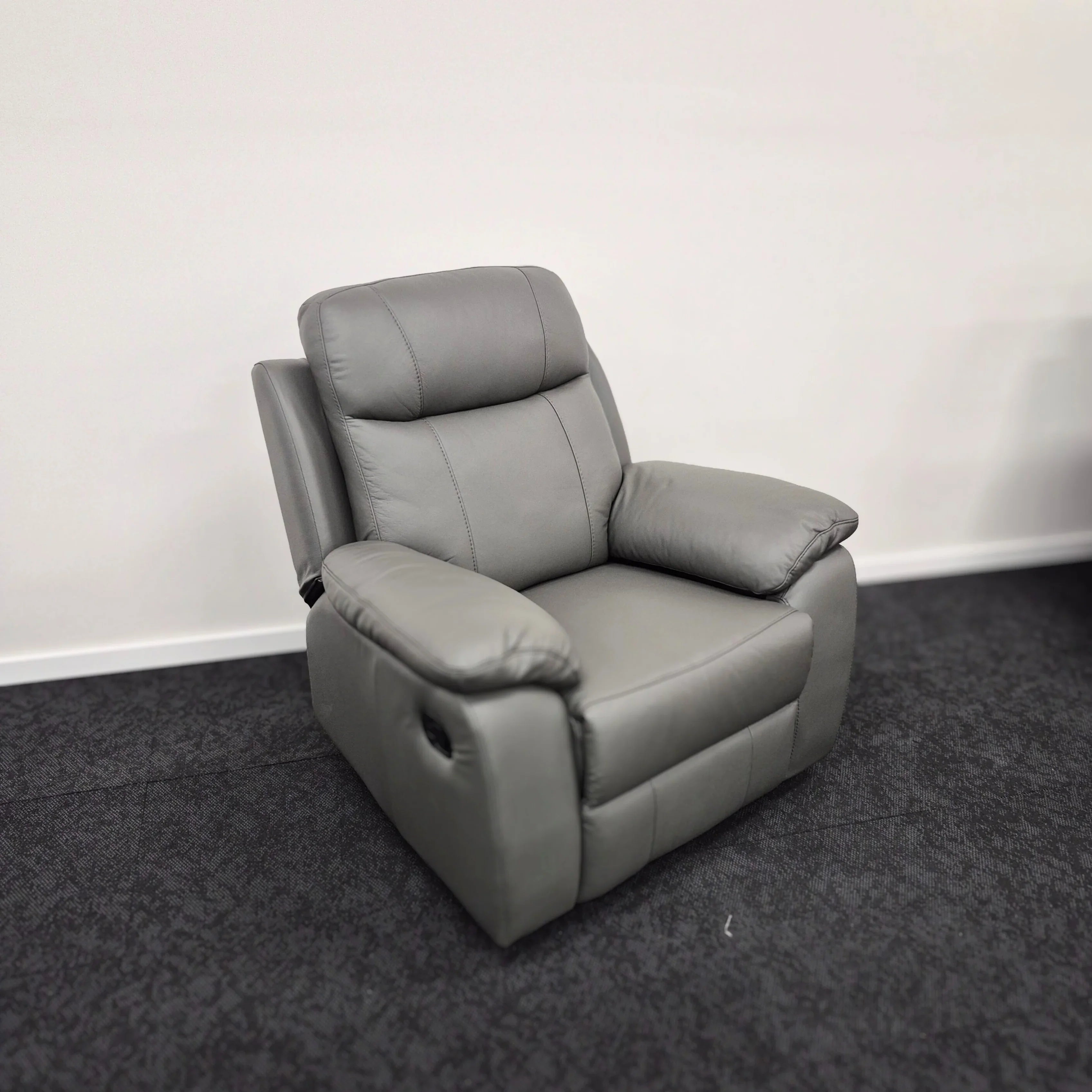 Grey leather recliner armchair with padded cushions on a dark carpeted floor