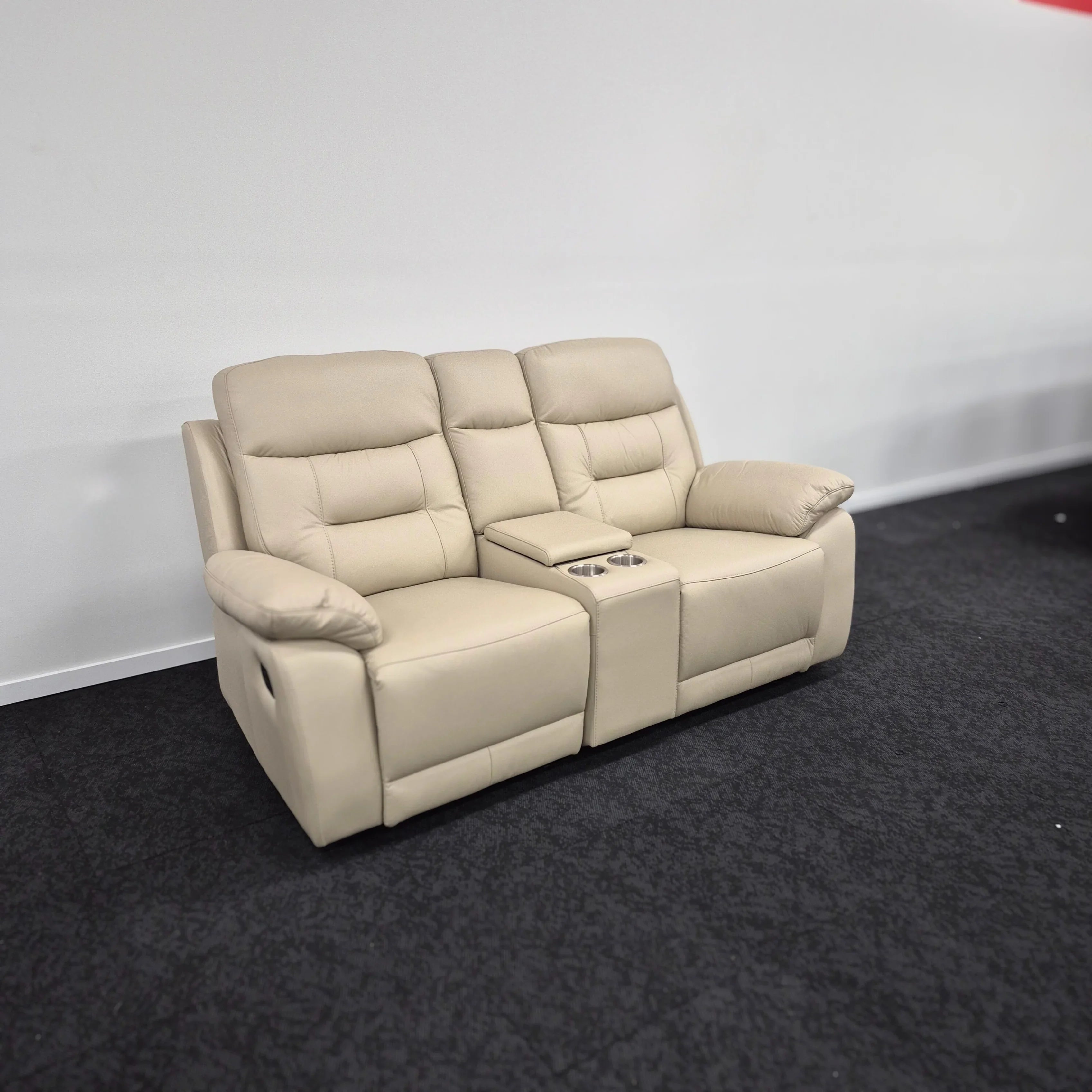 Beige leather 2-seater recliner sofa with cup holders and padded armrests on black carpet