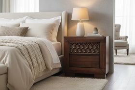 A bedroom with a wooden nightstand, a bed, a lamp and a bedside table with two drawers. 