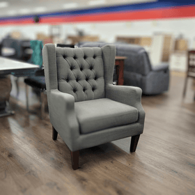 Grey tufted accent armchair with wooden legs on a showroom floor