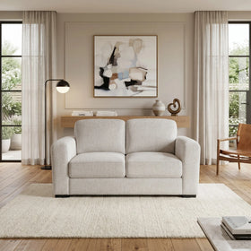 Montana 2 Seater Fabric Sofa in light beige fabric, set in a modern living room with neutral decor, wooden flooring, and soft natural lighting.
