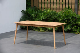 Rectangular outdoor wooden dining table on patio with modern slatted fence and greenery.