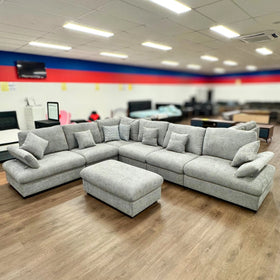 Large grey fabric modular sectional sofa with ottoman and cushions in a showroom
