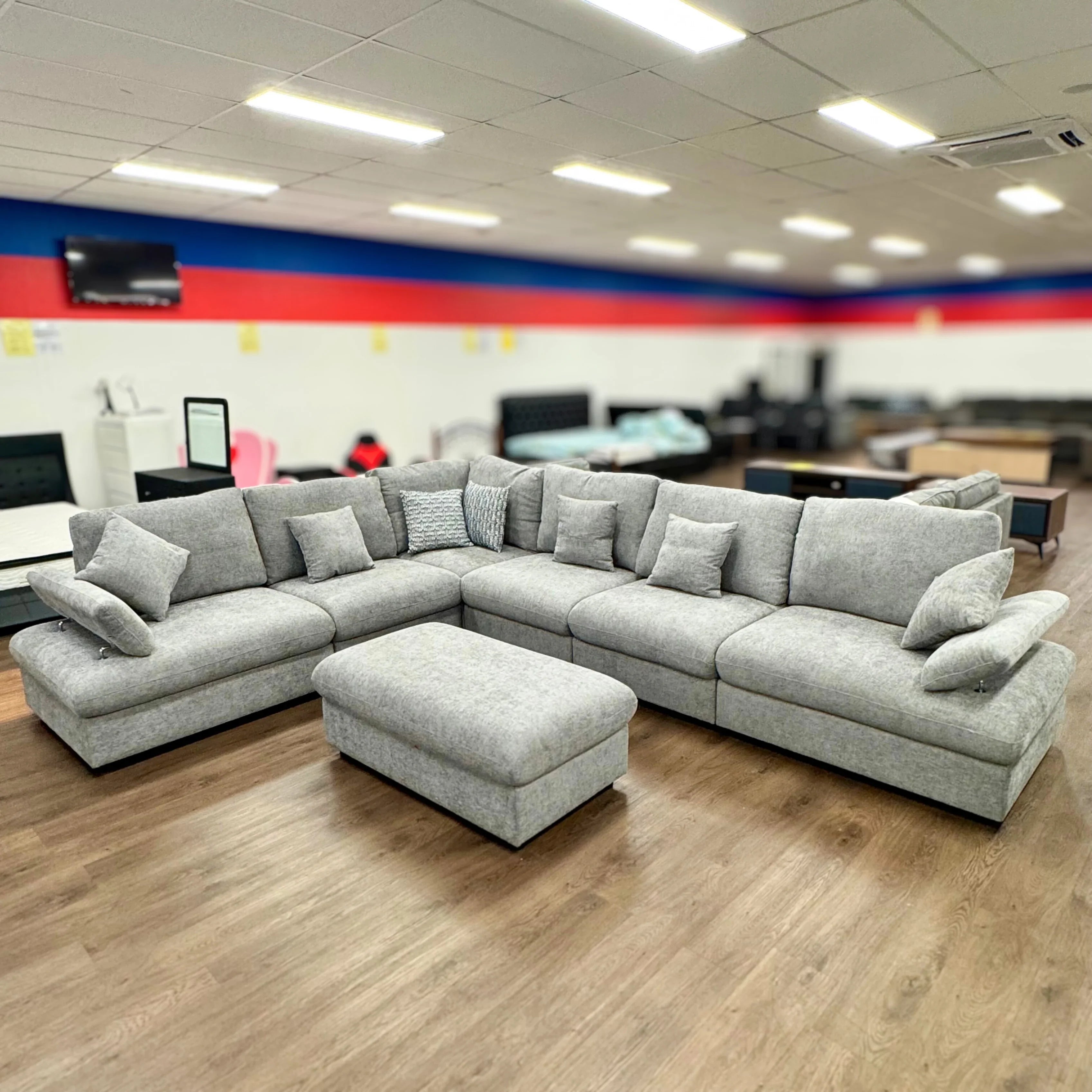 Large grey fabric modular sectional sofa with ottoman and cushions in a showroom