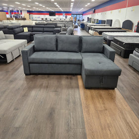 Oasis Pull Out Sofa Bed in dark grey fabric, front view in sofa mode with the storage chaise on the right, on display at The A2Z Furniture showroom
