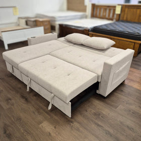 Beige sofa bed with tufted upholstery, extended flat with pillows, on wood floor in showroom