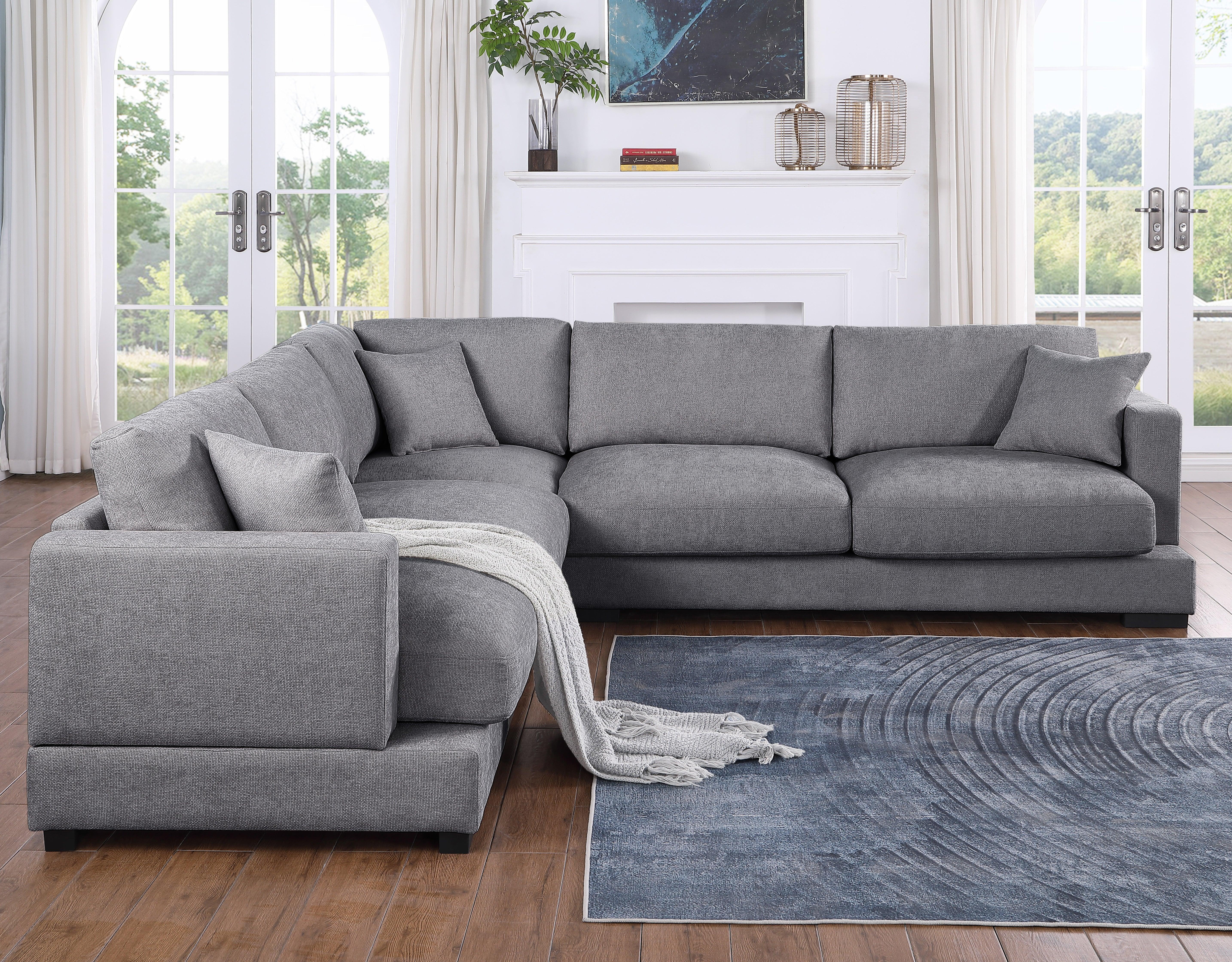 Grey sectional sofa with cushions and throw blanket in a bright living room with wood flooring